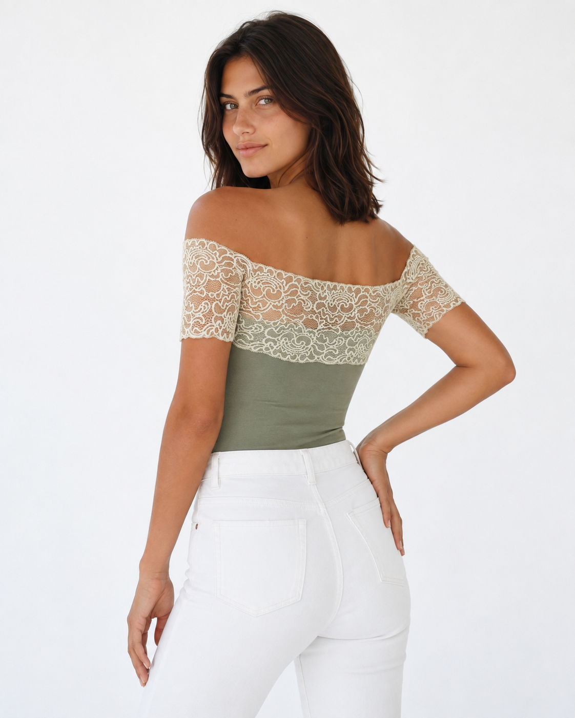 A woman modeling an off-the-shoulder top with a sage green body and beige lace sleeves, paired with white pants, against a plain white background.